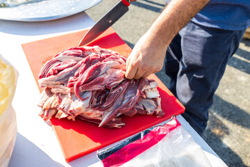 Male hands cutting meat into large pieces with a knife for pilaf.