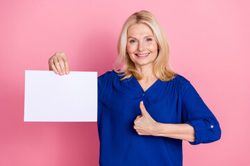 Photo portrait of attractive retired woman hold white paper sheet thumb up dressed stylish blue clothes isolated on pink color background