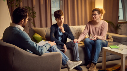 Psychologist leads therapy session with mother and her teenage son, discussing family issues in...