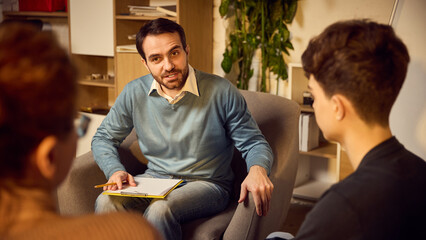 Man, psychologist engaged in productive discussion with teenage boy and his mother during family...