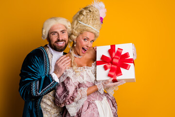 Elegant Couple in Historical Costumes Enthusiastically Posing With a Gift Box Against a Bright...