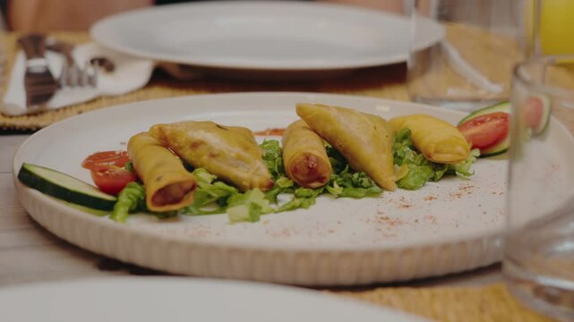 Delicious Moroccan pastilla and briouat served on a plate with fresh salad and tomato, with glasses and plates in the background. This traditional Moroccan dish, restaurants,