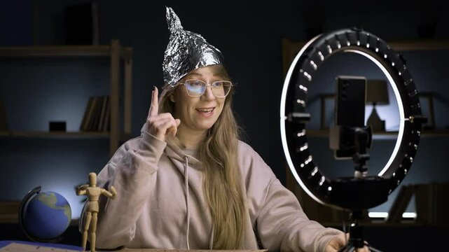 Strange crazy vlogger with cellphone, paranoid woman streaming at home conspiracy theory broadcasting in vlog, showing good idea gesture with finger-up. blogging and conspiracy theory