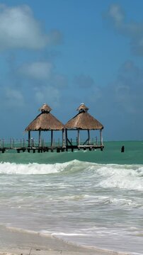 vertical video of blue clear ocean waves crashing on the sand with bamboo hut in tropical Cancun Mexico 