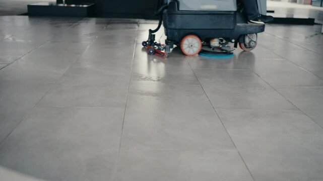 A person uses a floor scrubber to clean a tiled floor. The machine leaves the floor shiny and clean. Perfect for cleaning services, hygiene, and maintenance projects.