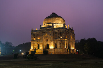 Obraz premium Illuminated ancient tomb with a large dome and intricate architecture at night, Lodi Garden, Delhi, India.