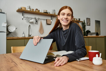 A stylish young guy with long hair smiles while engaged in activities at his modern home.