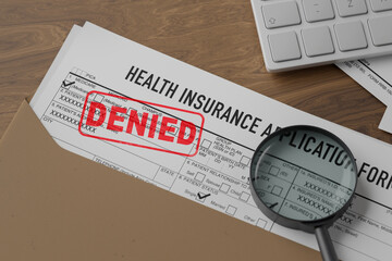 Denied health insurance application form on the table. Document with denied stamp put on the wooden...
