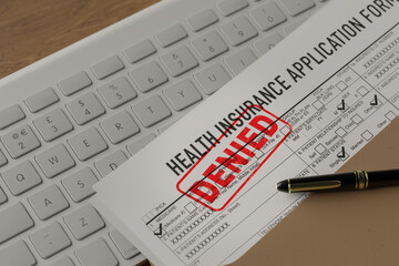 Document with denied stamp put on the wooden table.deneid health insurance application form on the...