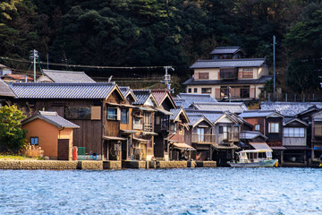 Fototapeta premium Traditional Wooden Boat Houses Along the Waterfront with Golden Light at Afternoon in Ine, Kyoto, Japan