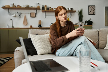 A young man in a sweatshirt sits comfortably in his modern apartment while checking his phone.