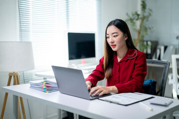 A woman is sitting at a desk with a laptop and a stack of papers