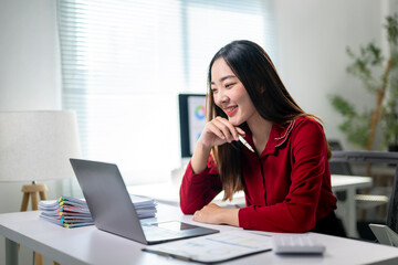 Obraz premium A woman is sitting at a desk with a laptop and a stack of papers
