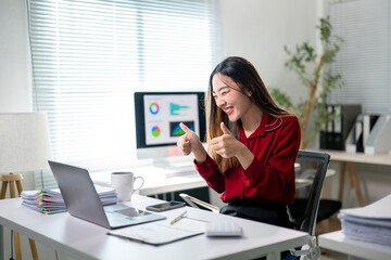 Obraz premium A woman in a red shirt is sitting at a desk with a laptop and a monitor