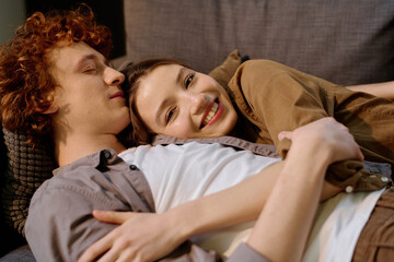 Medium close up of attractive young adult woman lying on boyfriends chest while he sleeping, she smiling widely and looking at camera