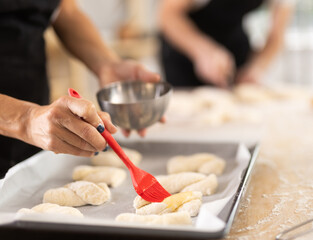 Female hands brushing uncooked dough pieces on baking sheet with oil before baking in oven closeup