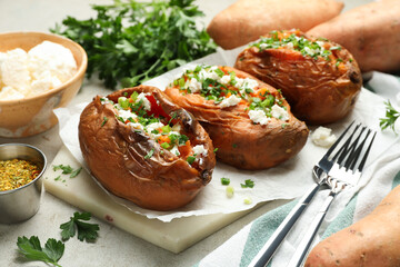 Tasty cooked sweet potatoes with feta cheese, green onion and parsley served on gray textured table, closeup