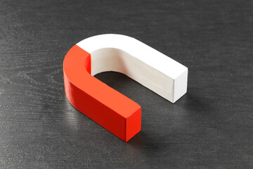 One horseshoe magnet on black wooden table, closeup