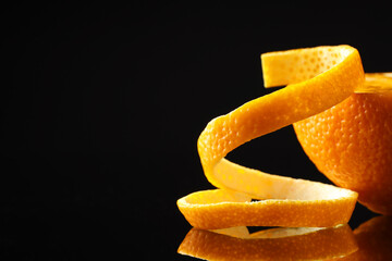 Fresh orange peel and half of fruit on black mirror surface, closeup. Space for text