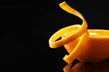 Fresh orange peel and half of fruit on black mirror surface, closeup. Space for text