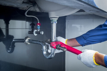 Plumber hands holding wrench doing repairing work at the sink and clogged pipe in bathroom carefully