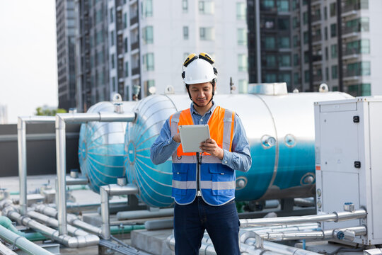 Male engineer work using digital tablet for checks or maintenance in sewer pipes area at construction site. Male plumber working in sewer pipes area at rooftop of building