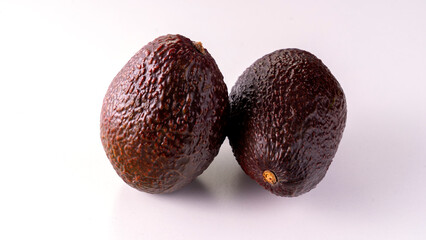 Two avocados are sitting on a white background. They are both brown and have a rough texture