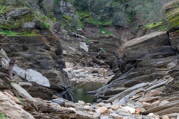 Rocky canyon in Monfragüe's circular route to Cerro Gimio, Cáceres, Spain. Natural beauty with green moss, rugged cliffs, and serene water reflections in a pristine environment
