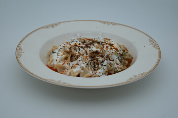 Traditional Turkish dish meat manti served in a white plate with yoghurt, mint and red pepper