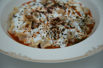 Traditional Turkish dish meat manti served in a white plate with yoghurt, mint and red pepper