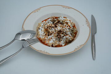 Traditional Turkish dish meat manti served in a white plate with yoghurt, mint and red pepper