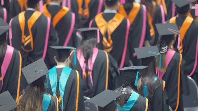 A group of people wearing graduation gowns and caps. The gowns are orange and blue. The people are standing in a line