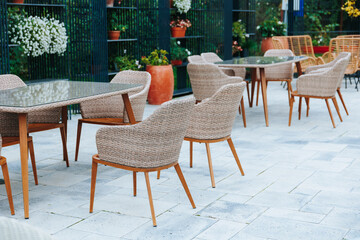 Wicker chairs and glass-top tables in a cozy outdoor dining area with greenery.