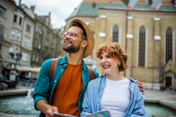 Young couple exploring the new city. Hugging and walking through the center. Wearing hats and backpacks.