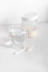 Glass of water, jar with powder and measuring spoon on white background. Vertical. Protein or collagen