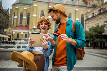 Happy couple on vacation ordering online with credit card on their tablet.