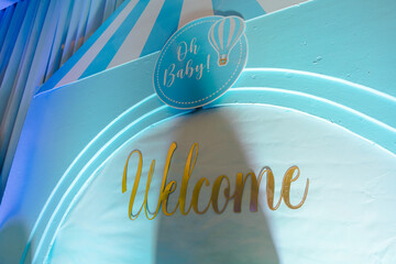 Welcome Baby! A whimsical, light blue baby shower backdrop featuring a hot air balloon and gold lettering.