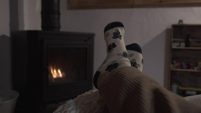 horizontal video of bare feet of a woman with patterned sock resting on a pouf in front of a wood fireplace