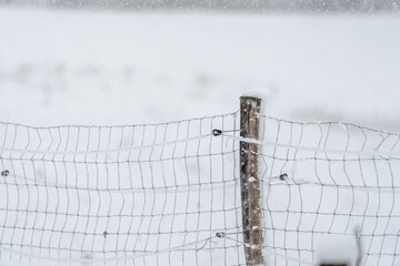 A fence covered in snow with a wooden post sticking out of it