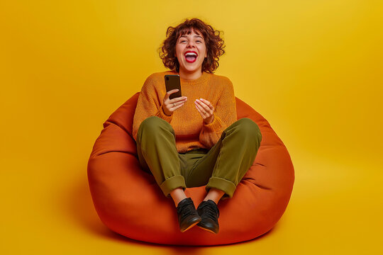 Young woman dressed casually, laughing and holding a phone, seated on an orange beanbag against a vibrant yellow backdrop. Expressing fun, relaxation, and joy in a casual and trendy style.