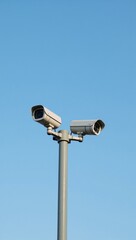 Two camera poles stand watch over a peaceful blue sky offering heightened surveillance and safety in a bustling public area