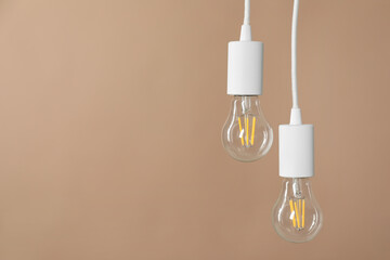 Light bulbs hanging on cords against beige background, space for text