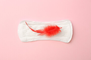 Menstrual pad with red feather on light pink background, top view