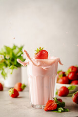 Glass of fresh strawberry splashing milkshake, smoothie and fresh strawberries on light background. Healthy food and drink concept.