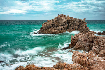 waves crashing against a rock, large rock in the sea with cormorants perched on it