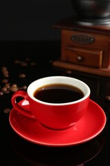 Red cup with coffee, vintage grinder and roasted beans on black background