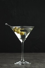 Martini cocktail with olives in glass on grey table against black background