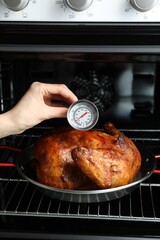 Woman measuring temperature of delicious baked turkey in kitchen, closeup