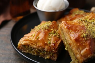 Delicious baklava with crushed nuts and ice cream on wooden table, closeup