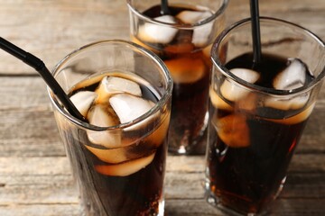 Refreshing cola with ice cubes and drinking straws in glasses on wooden table, closeup
